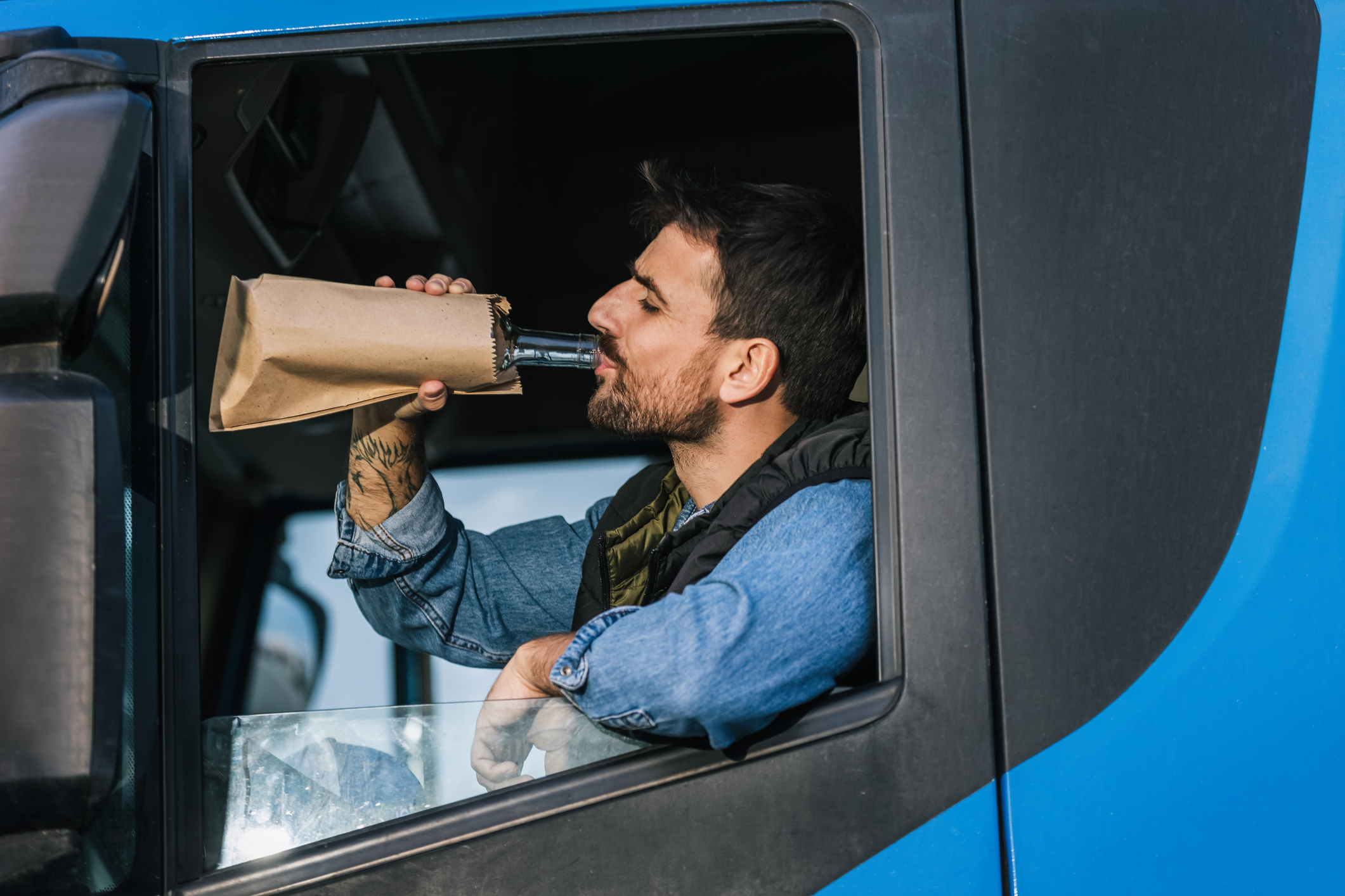 Young handsome man driving long vehicle, taking a break from long ride and drinking some alcohol.